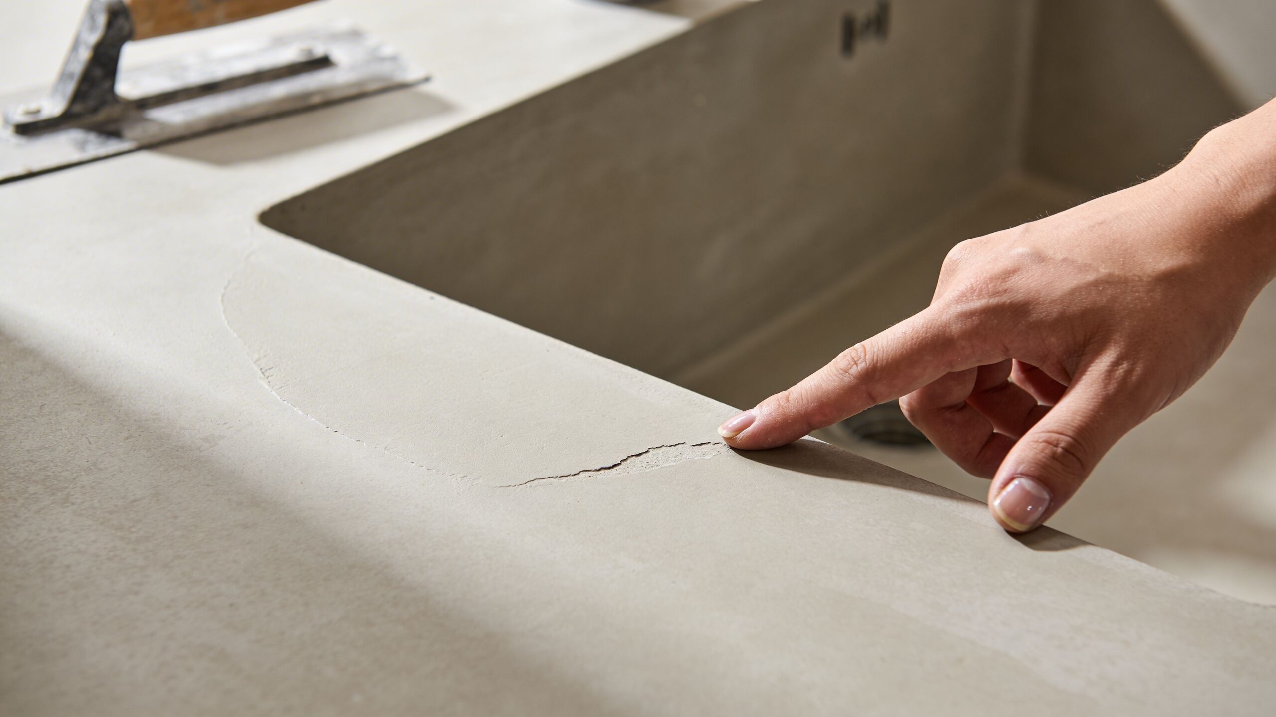 En person peger på en revne i en bordplade lavet af mikrocement under renovering af et køkken.