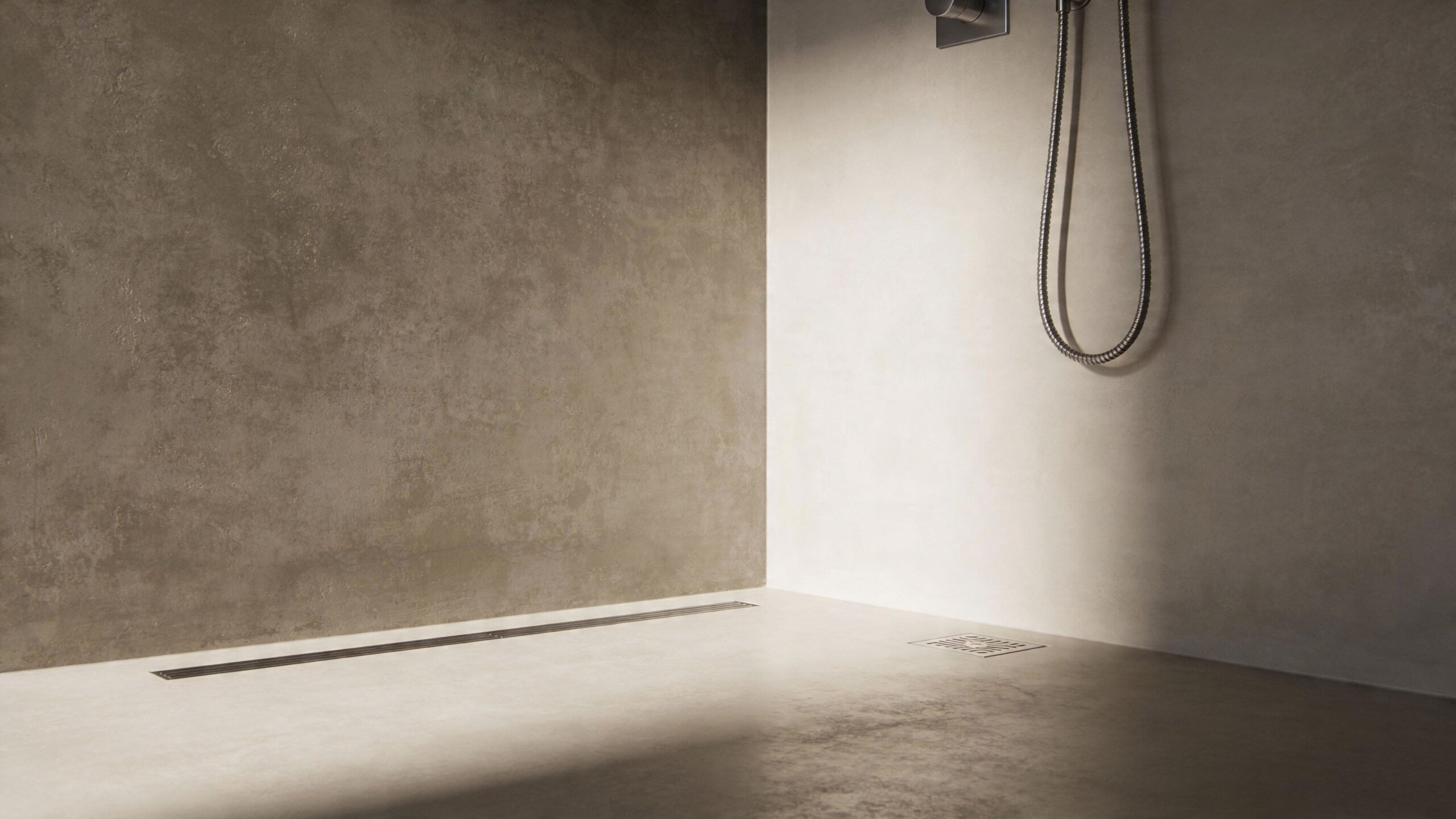 Moderne brusebad med betonvægge, en lang afløbsrist og et minimalistisk brusesystem i et stilfuldt badeværelsesmiljø.