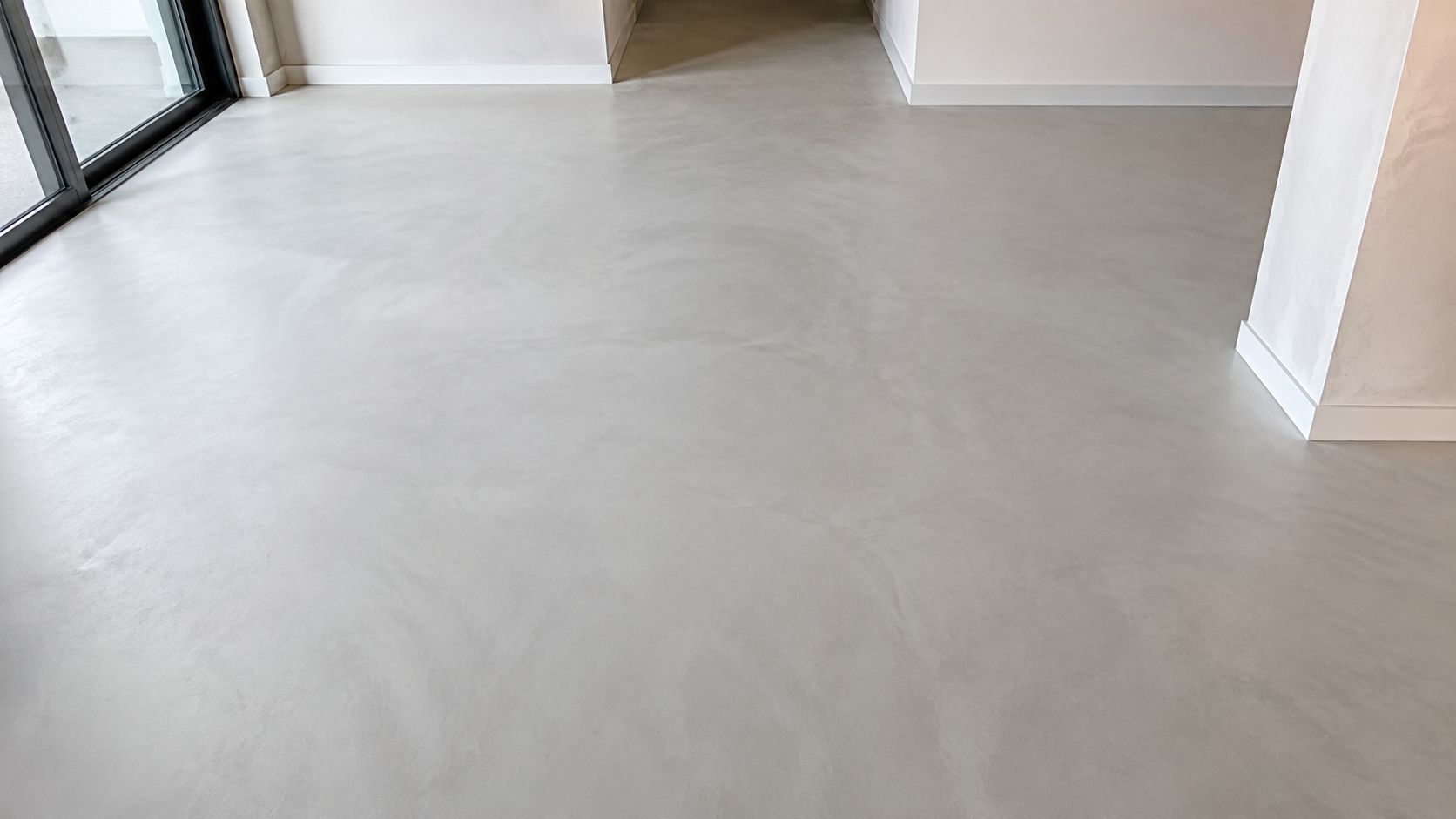 Moderne interiør med et flot og jævnt lysegråt betonspartel gulv i et åbent og lyst rum.